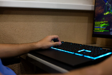 Close up shot of person hand using modern illuminated gaming keyboard during video game session. The dynamic lighting and the screen display enhance the immersive experience