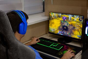 Person playing online video game on computer, using gaming headset, keyboard and mouse. The screen shows action packed scene from role playing game