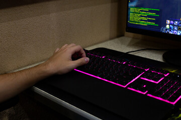 Close up of gamer hand on keyboard, featuring vibrant pink backlighting. Screen in background shows gaming interface, highlighting immersive experience of digital gaming