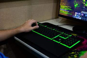 Hand on glowing keyboard, focused on computer game. Illuminated keys contrast with dark environment, symbolizing deep immersion into digital worlds and impact of screen time