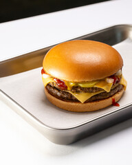 Classic double cheeseburger with melted cheese, ketchup, and pickles on a metal tray.