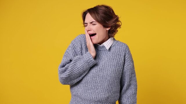 Tired young woman wear grey sweater white shirt casual clothes did not get enough sleep last night after party and barely got up in the morning yawning rubs eyes isolated on plain yellow background