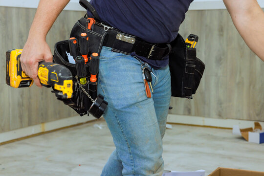 Construction worker is actively using power drill in home under renovation, using tool belt equipment.