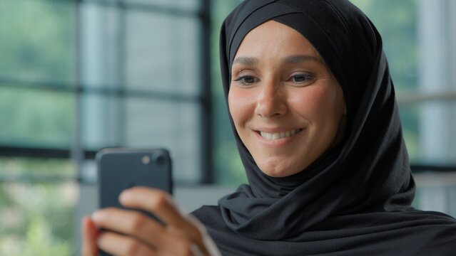Close-up smiling Muslim business woman in hijab chatting mobile phone Arabian businesswoman female girl happy smile using smartphone at workplace worker scrolling online social media company web chat - Powered by Adobe