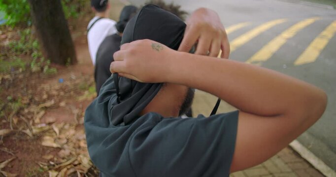 African American man adjusting durag on head beside city street and sports field, representing self-expression, cultural identity, and quiet confidence in urban daily life