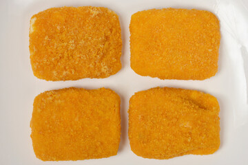 A studio image of four pieces of uncooked, breaded Trappist cheese arranged on a white plate