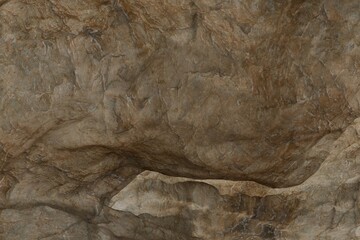 Textured natural stone surface in earthy brown-tan tones, featuring rugged cracks, ridges, and...