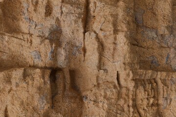 Detailed view of a natural, rough rock or stone wall, showcasing deep crevices, varied textures, and earthy tones with hints of gray and blue