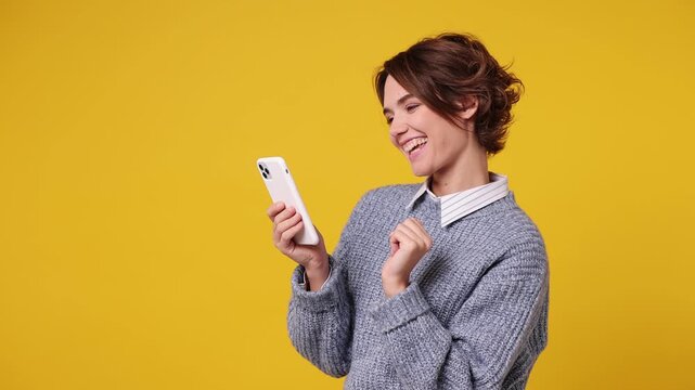 Young woman wear grey sweater shirt casual clothes hold use mobile cell phone typing swipe chat send sms doing online shopping order delivery to home booking tour isolated on plain yellow background