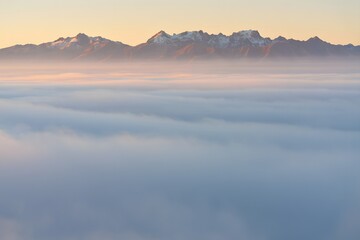Obraz premium Mountains peeking through the clouds during a golden sunset in a serene landscape