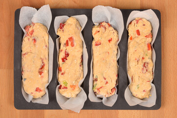 Four loaves of unbaked savory bread dough, mixed with chopped red Macedonian peppers and other ingredients, are ready to be baked in a baking mold on a wooden surface.