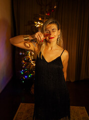 Woman toasting with champagne by a Christmas tree on New Year&rsquo;s Eve