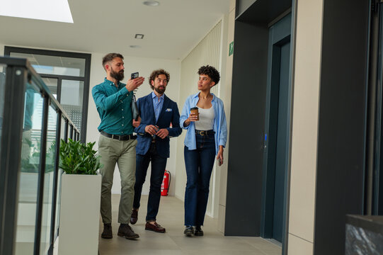 Businesspeople are walking down an office corridor, one of them showing something on his phone to the others, while a woman holds a takeaway coffee cup - Powered by Adobe