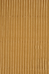 A vertical full-frame macro shot captures the repeating pattern and texture of vertical ridges on a sheet of metallic gold corrugated cardboard