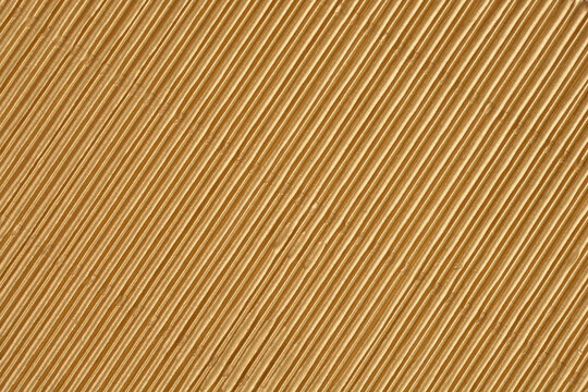 A full-frame macro shot captures the repeating texture of fine, diagonal ridges on a sheet of shiny metallic gold corrugated cardboard - Powered by Adobe