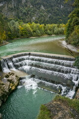 Obraz premium The stunning stepped weir of the Lechfall near Füssen, Bavaria, showcasing the turquoise waters of the Lech River and autumn foliage.