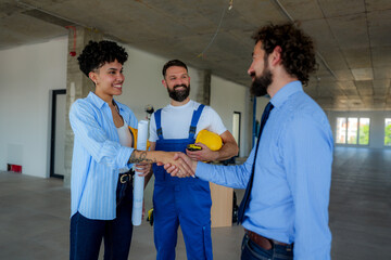 Architect and businessman shaking hands in front of a construction worker holding a yellow helmet,...