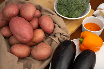 Fresh potatoes, broccoli, eggplants, and orange bell pepper on a wooden table. Colorful vegetables for healthy cooking. Healthy eating