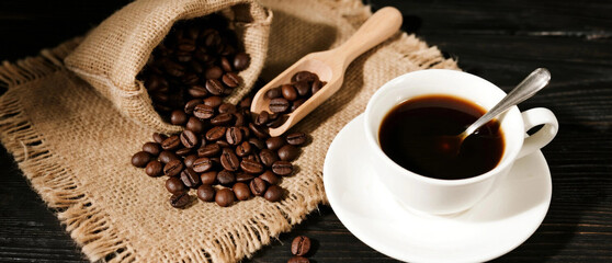 Fresh black coffee in white cup with roasted beans and wooden scoop on rustic dark table