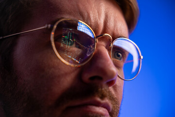 Close-up of an ambitious trader analyzing financial data, reflection of stock charts in glasses, symbol of success, focus, and determination in business and finance. Copy space, blue background.