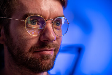 Close-up portrait of a crypto trader monitoring bitcoin chart, financial chart reflection in glasses, success, ambitions in dim shadowy lighting, blue background and with copy space.
