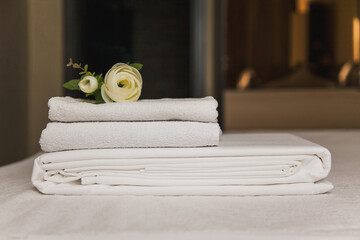Towels and linens neatly arranged on a bed with a decorative flower accent
