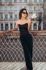 Stylish woman in black jumpsuit standing straight on balcony