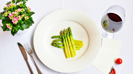 asparagus in a white plate on a table with a glass of wine and flowers