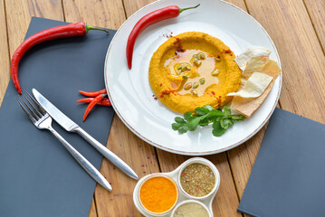 hummus in a white plate with chili pepper on the table