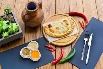 Khachapuri with meat on a wooden board on parchment on a table with chili pepper and decoration
