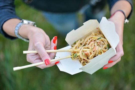 A girl with chopsticks holds noodles with crayfish in a disposable container