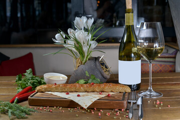 large kebab on a wooden board with pita bread and herbs on a table with white wine