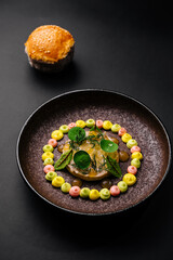 Unique circular dish with colorful garnishes and a bread roll in a dark setting
