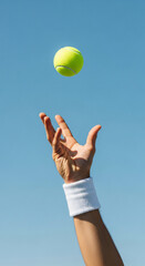 Energetic male hand tossing yellow tennis ball, clear blue sky