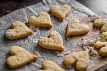 Heart-shaped cookies arranged on parchment paper, dusted with flour, evoke warmth and sweetness.