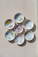 Collection of seven vintage floral porcelain saucers displayed in a decorative circular arrangement on a pastel wall.