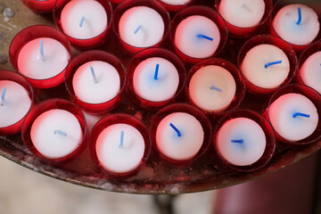 Red votive candles with blue wicks arranged neatly in a circular holder, viewed from above.