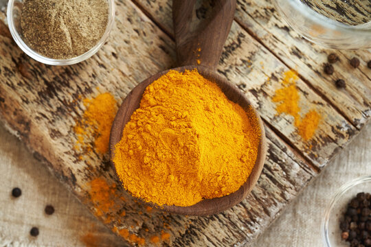 Dry turmeric root powder in a spoon with ground and whole black pepper