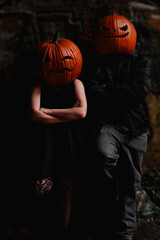 Quirky couple in pumpkin heads poses against an urban backdrop during Halloween night