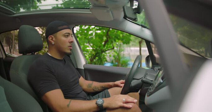 Latin Hispanic man sitting quietly inside parked car, looking out through windshield with calm and reflective expression, appearing lost in thought or waiting in traffic