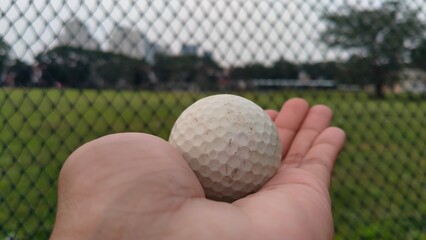 close up of a hand holding a golf ball with a golf course in the background