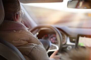 Young girl drives a car on the highway in the afternoon sun.