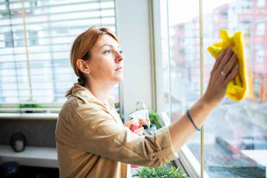 Middle aged woman cleaning window at home