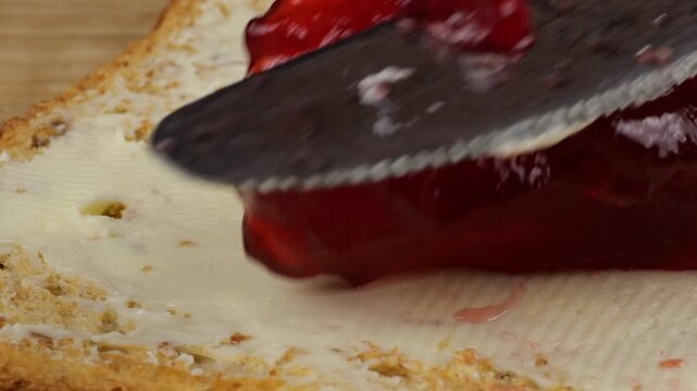 Spread redcurrant jam on a slice of toasted bread with butter using a knife.