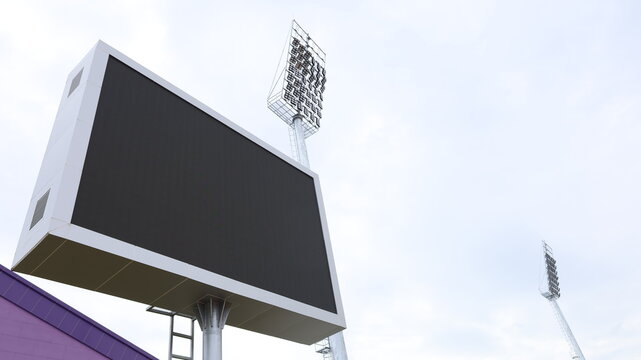 Outdoor advertising LED billboard. A large outdoor black scoreboard with spotlights on the side of a stadium against a white sky background and copy space. Selective focus.