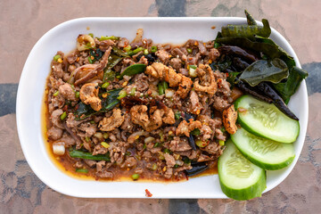 Spicy minced meat salad (Larb) with herbs, crispy pork, and cucumber on a white plate.