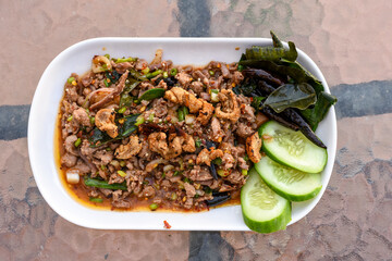 Spicy minced meat salad (Larb) with herbs, crispy pork, and cucumber on a white plate.