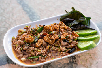 Spicy minced meat salad (Larb) with herbs, crispy pork, and cucumber on a white plate.