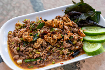 Spicy minced meat salad (Larb) with herbs, crispy pork, and cucumber on a white plate.