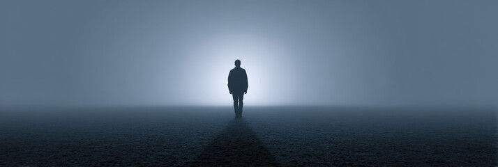 Silhouette of man walking alone into dark fog toward mysterious light. lonely, conceptual journey into an unknown future filled with mystery and emotion